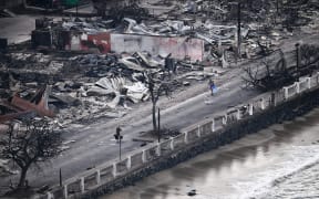 An aerial image taken on August 10, 2023 shows a person walking down Front Street past destroyed buildings burned to the ground in Lahaina in the aftermath of wildfires in western Maui, Hawaii. At least 36 people have died after a fast-moving wildfire turned Lahaina to ashes, officials said August 9, 2023 as visitors asked to leave the island of Maui found themselves stranded at the airport. The fires began burning early August 8, scorching thousands of acres and putting homes, businesses and 35,000 lives at risk on Maui, the Hawaii Emergency Management Agency said in a statement. (Photo by Patrick T. Fallon / AFP)
