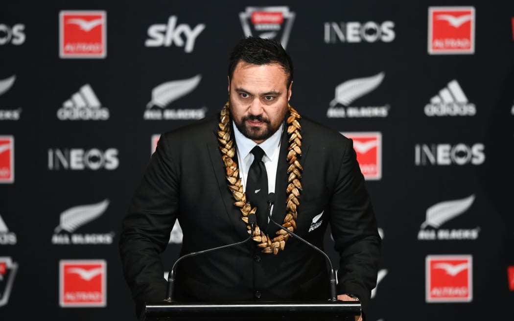 A photo of All Blacks board member Bailey Mackey reading out the names of the All Blacks Squad for the July 2022 Test Series against Ireland. Mangere, Auckland, New Zealand on Monday 13 June 2022. He is standing at a podium with the All Black branding behind him.