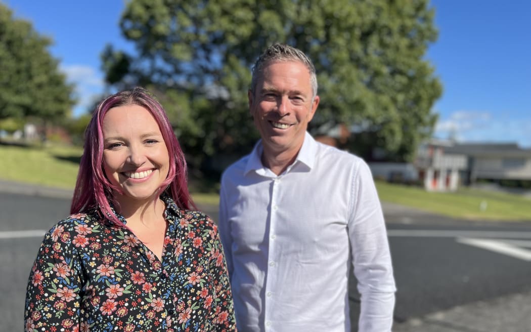 Nancy Baines and Nick Brown stand on a suburban street corner on a sunny day.