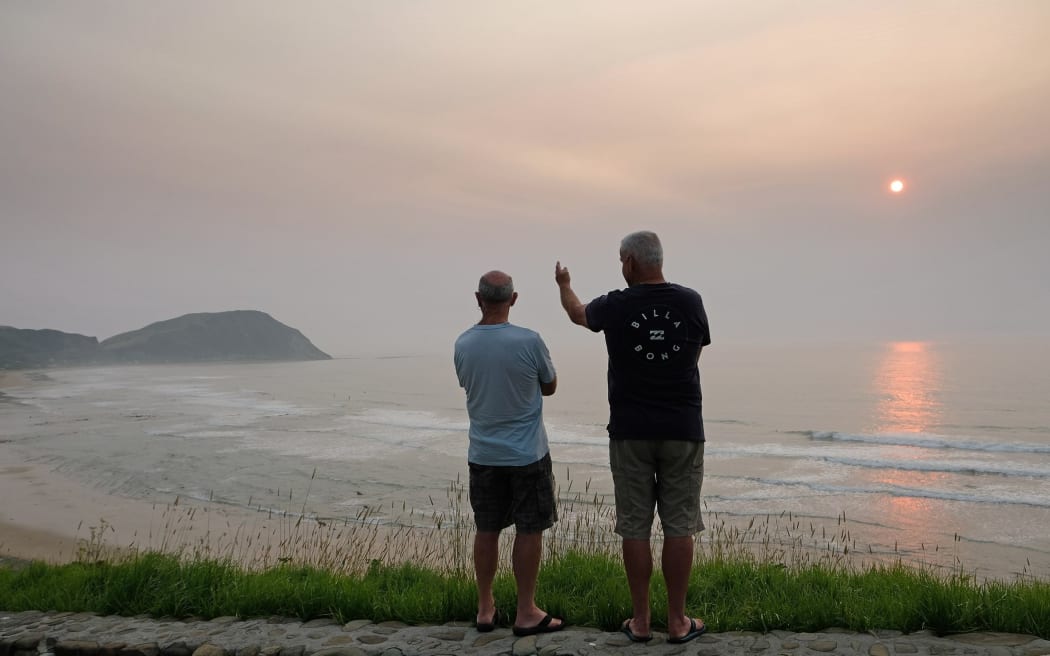 Two surfers look out across Makorori Beach near Gisborne where smoke haze from the Australia bushfires has cloaked the east coast in an fog-like haze turning the rising sun red.