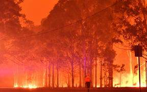 A firefighter walks past burning trees during a battle against bushfires around the town of Nowra in the Australian state of New South Wales on December 31, 2019.