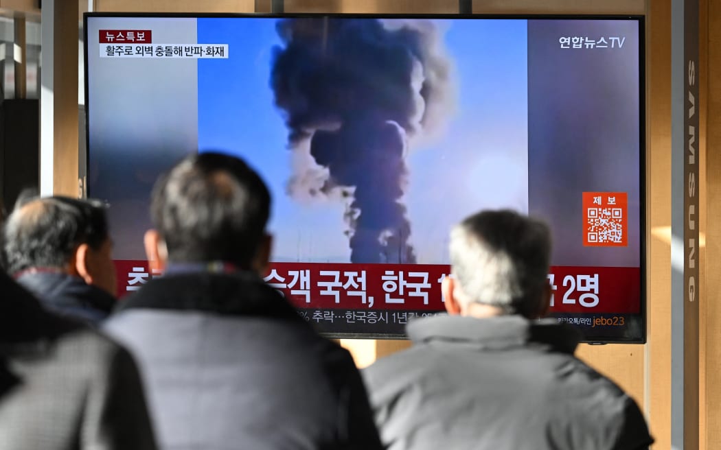 People watch a television screen broadcasting footage of an airplane crash at Muan international airport, at a train station in Seoul on December 29. 2024. - A plane carrying 181 people crashed at Muan international airport in South Korea on December 29, killing at least 29 people, authorities told AFP. (Photo by JUNG YEON-JE / AFP)