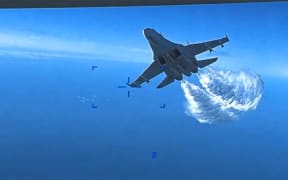 This handout image taken from video released by US European Command (USEUCOM) on 16 March, 2023,  shows onboard footage from a US Air Force MQ-9 drone as it is approached the first time by a Russian SU-27 aircraft jettissoning fuel over The Black Sea on 14 March, 2023.