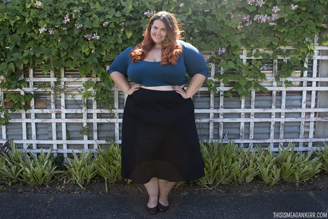 A portrait of Meagn Kerr standing in front of a garden wearing a black skirt and green crop top.