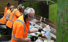 Workers manually separate the recycled items coming in on a conveyer belt.