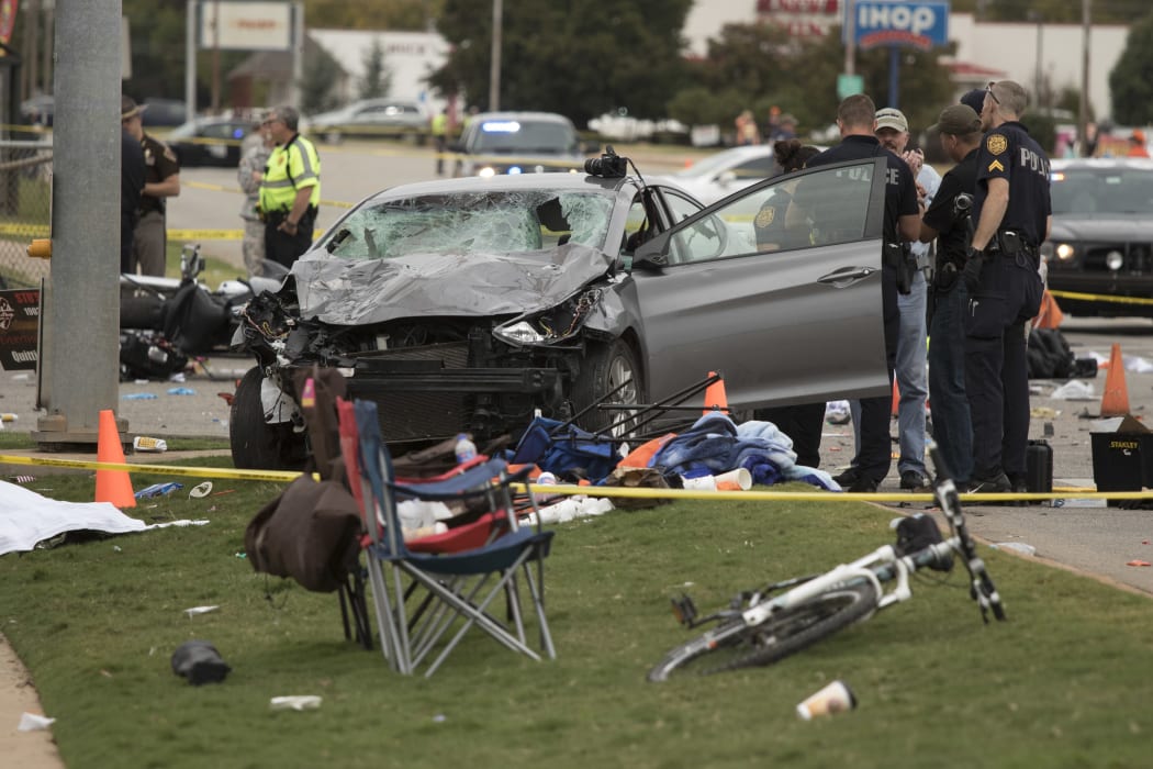 Emergency officials stand over the car that was involved after a suspected drunk driver crashed into a crowd of spectators during the Oklahoma State University homecoming parade.