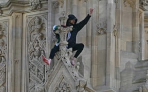 A protester holding a Palestinian flag gestures from the side of the Elizabeth Tower, commonly known by the name of the clock's bell "Big Ben", at the Palace of Westminster, home to the Houses of Parliament, in central London, on March 8, 2025. UK police closed the area around Big Ben in London on Saturday after a man holding a Palestinian flag climbed the tower housing the famous bell. The man climbed several metres up the Elizabeth Tower and stood barefoot on a ledge holding the flag, according to witnesses. (Photo by Ben STANSALL / AFP)
