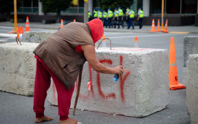 Protester spray paints concrete barriers put in place by police.