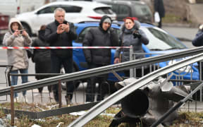 People stand behind the cordoned off area around the remains of a shell in Kyiv on February 24, 2022