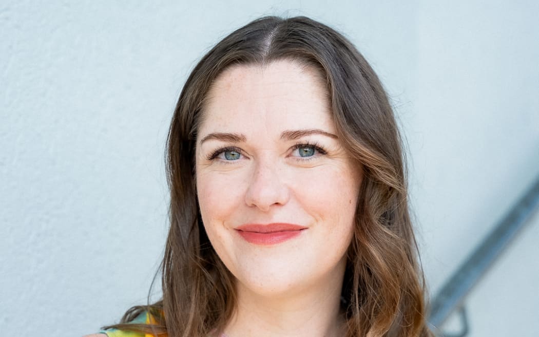 This is a headshot of Jessica Lockhart. She is looking towards the camera. Her brown hair frames her face. She has blue eyes and red lips drawn in a thin smile.