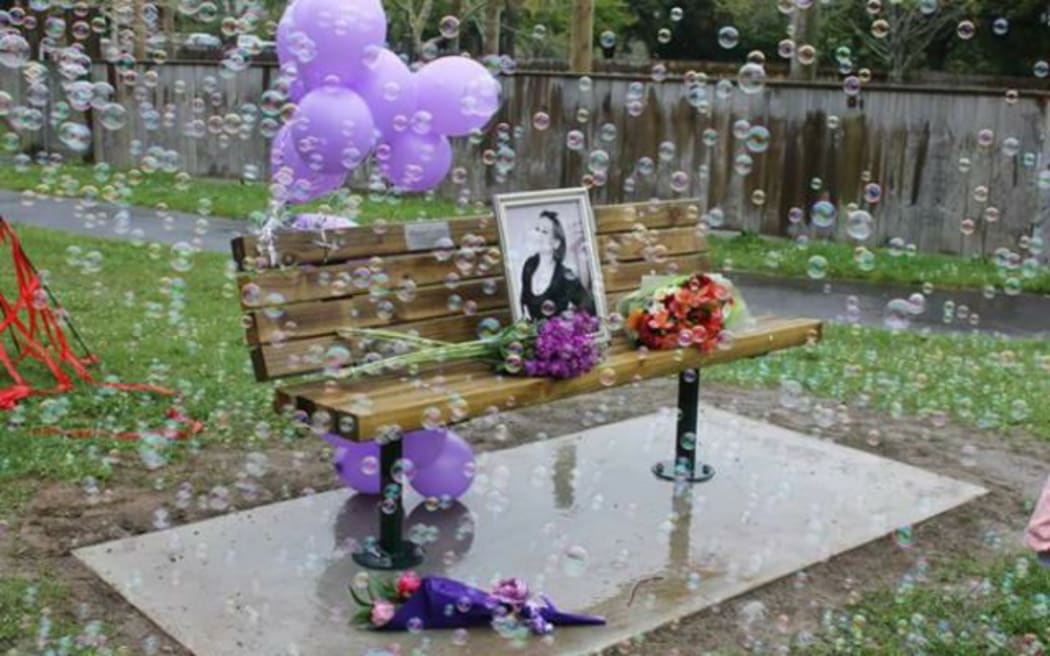 A photo of Lois Tolley on a bench that carries a plaque from family and friends in her memory.