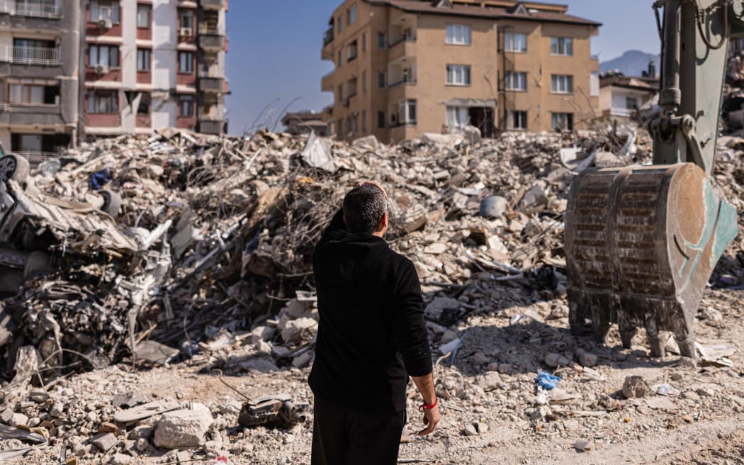A man stands in front of collapsed buildings in Antakya, southern Turkey on 20 February 2023. The buildings were destroyed in the deadly 6 February 7.8 and  7.5-magnitude quakes.