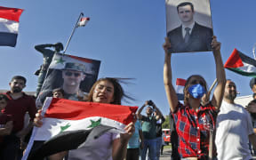 People wave Syrian national flags and pictures of President Bashar al-Assad during a demonstration in support of Assad and against US sanctions on the country, at the Umayyad Square in the centre of the capital Damascus on June 11, 2020.