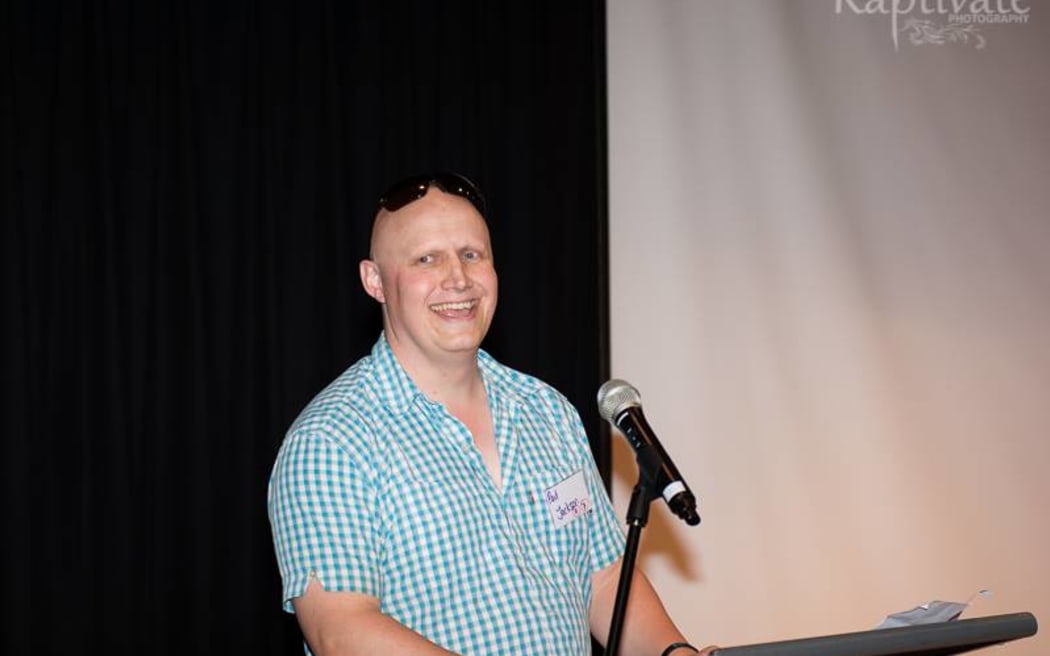 Paul Jackson of AlopeciaNZ stands in front of a microphone.