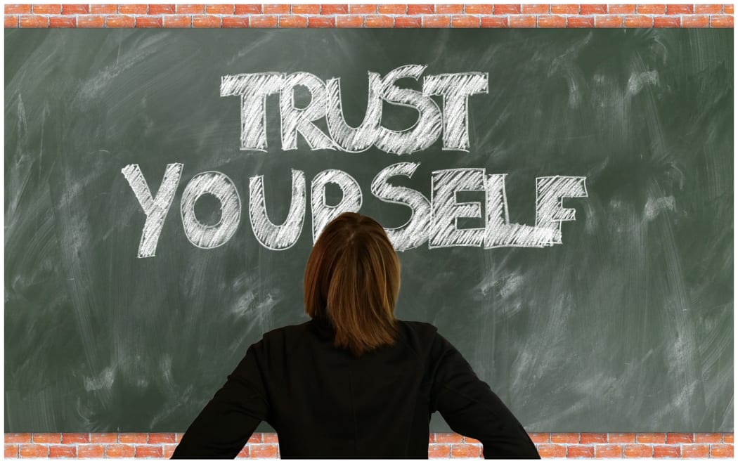 Young person standing in front of a blackboard saying 'Trust Yourself'