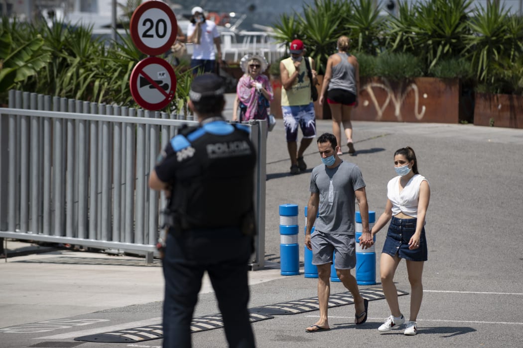 People stroll at Barcelona's harbour as a local police officer watches, on July 18, 2020. Four million residents of Barcelona have been urged to stay at home as virus cases rise.