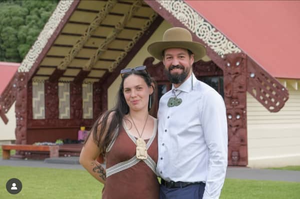 Sam Gibson and Roimata Sinclair stand together in front of a marae.