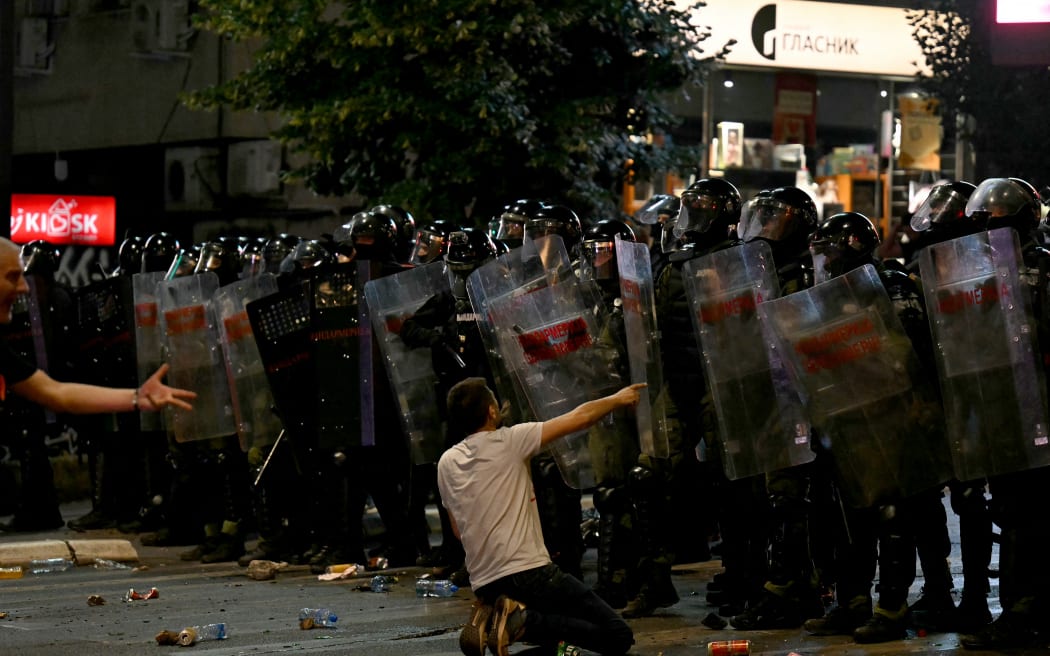 A protestor kneels in front of Serbian Riot Police during clashes after tens of thousands of protesters gathered in central Belgrade to issue an "ultimatum" to the populist government to call early elections after months of student-led strikes across the country, in Belgrade, on June 28, 2025. Anti-graft protests have rocked the Balkan nation since November when 16 people were killed in the northern city of Novi Sad by a train station roof collapse, a tragedy widely blamed on entrenched corruption. For over half a year, students have blockaded universities and organised large demonstrations around the country, demanding a transparent investigation into the tragedy with their focus shifting after little action from authorities to call for early parliamentary elections. (Photo by OLIVER BUNIC / AFP)