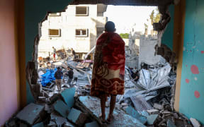 A youth draped in a blanket looks on as people look for survivors in the rubble of a building hit in an Israeli strike in the Bureij camp for Palestinian refugees in the central Gaza Strip on May 2, 2025. (Photo by Eyad BABA / AFP)