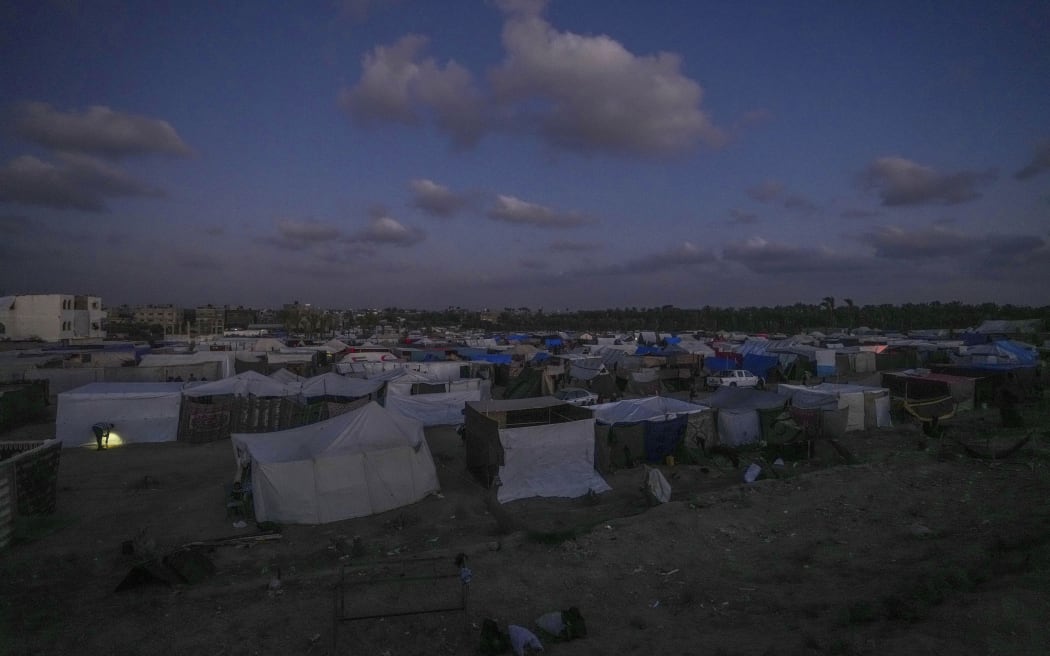 A Palestinian man (left), displaced by the Israeli air and ground offensive on the Gaza Strip, checks a makeshift tent during dusk at a camp in Deir al Balah, on 13 May, 2024.