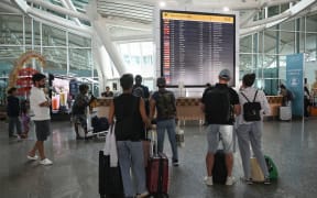 Passengers look at an electronic board displaying cancelled flights after the nearby Mount Lewotobi Laki-Laki volcano catapulted an ash tower miles into the sky, at the Ngurah Rai International Airport in Tuban near Denpasar, on Indonesia's resort island of Bali on November 13, 2024. (Photo by SONNY TUMBELAKA / AFP)