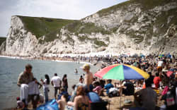 People relax in the sunshine on Durdle Door beach, east of Weymouth on the south coast of England on 23 May 2026, as temperatures are set to rise over the long bank holiday weekend. (Photo by Henry NICHOLLS / AFP)