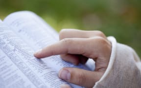 A file photos shows a woman's hand pointing to a Bible passage.