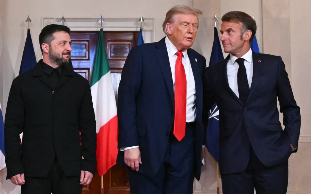 (L/R) Ukrainian President Volodymyr Zelensky, US President Donald Trump, and French President Emmanuel Macron stand for a family photo with European leaders in the Cross Hall of the White House in Washington, DC, on August 18, 2025. European leaders join Ukrainian President Volodymyr Zelensky in talks with US President Donald Trump on August 18, as they try to find a way to end Russia's offensive.  The leaders heading to Washington on Monday to appear alongside Zelensky call themselves the "coalition of the willing." (Photo by ANDREW CABALLERO-REYNOLDS / AFP)
