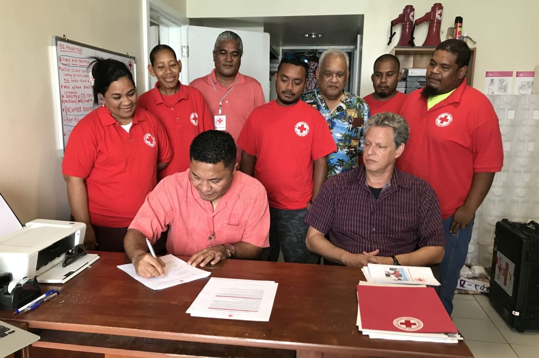 Marshall Islands Minister of Health Kalani Kaneko signs an agreement with the Marshall Islands Red Cross Society for cooperation in first aid training as Red Cross Secretary General Jack Niedenthal (sitting) and staff and volunteers look on.