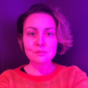 A woman is looking directly at the camera with illuminated by neon light