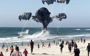 This image grab from an AFPTV video shows Palestinians running toward parachutes attached to food parcels, airdropped from US aircrafts on a beach in the Gaza Strip on March 2, 2024. Israel's top ally the United States said it began air-dropping aid into war-ravaged Gaza on March 2, as the Hamas-ruled territory's health ministry reported more than a dozen child malnutrition deaths.
