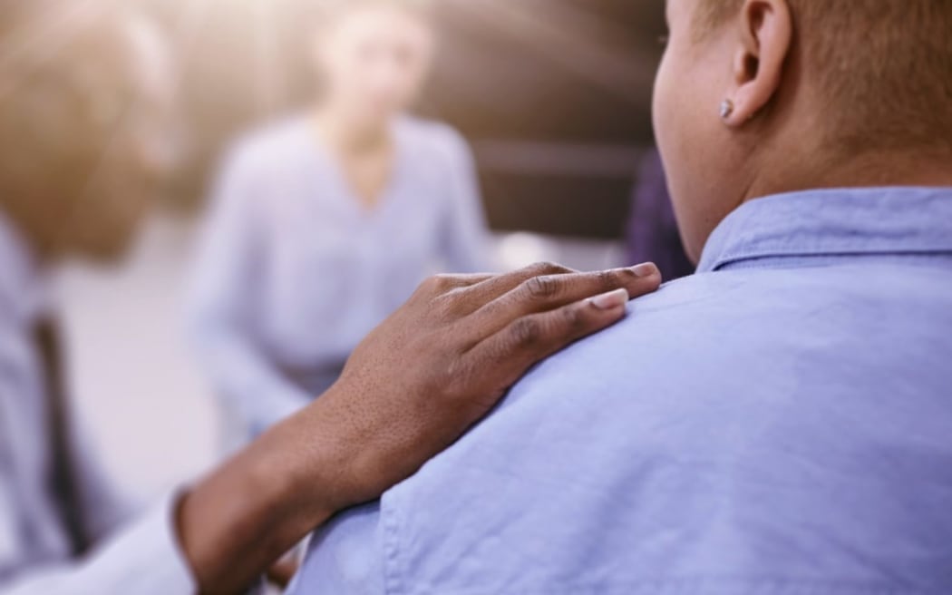 A hand is placed on a man's shoulder.