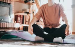 A person sitting with their legs crossed on a yoga mat.