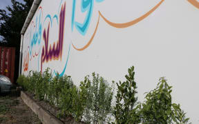 Plants in commemoration of the 51 lives lost in the Christchurch mosque shootings are put at Linwood Mosque underneath a mural of a saying from the Prophet.