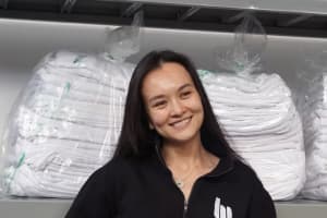Caroline Beuth is a smiling woman with long dark hair who stands in front of two bags of folded white clothing.
