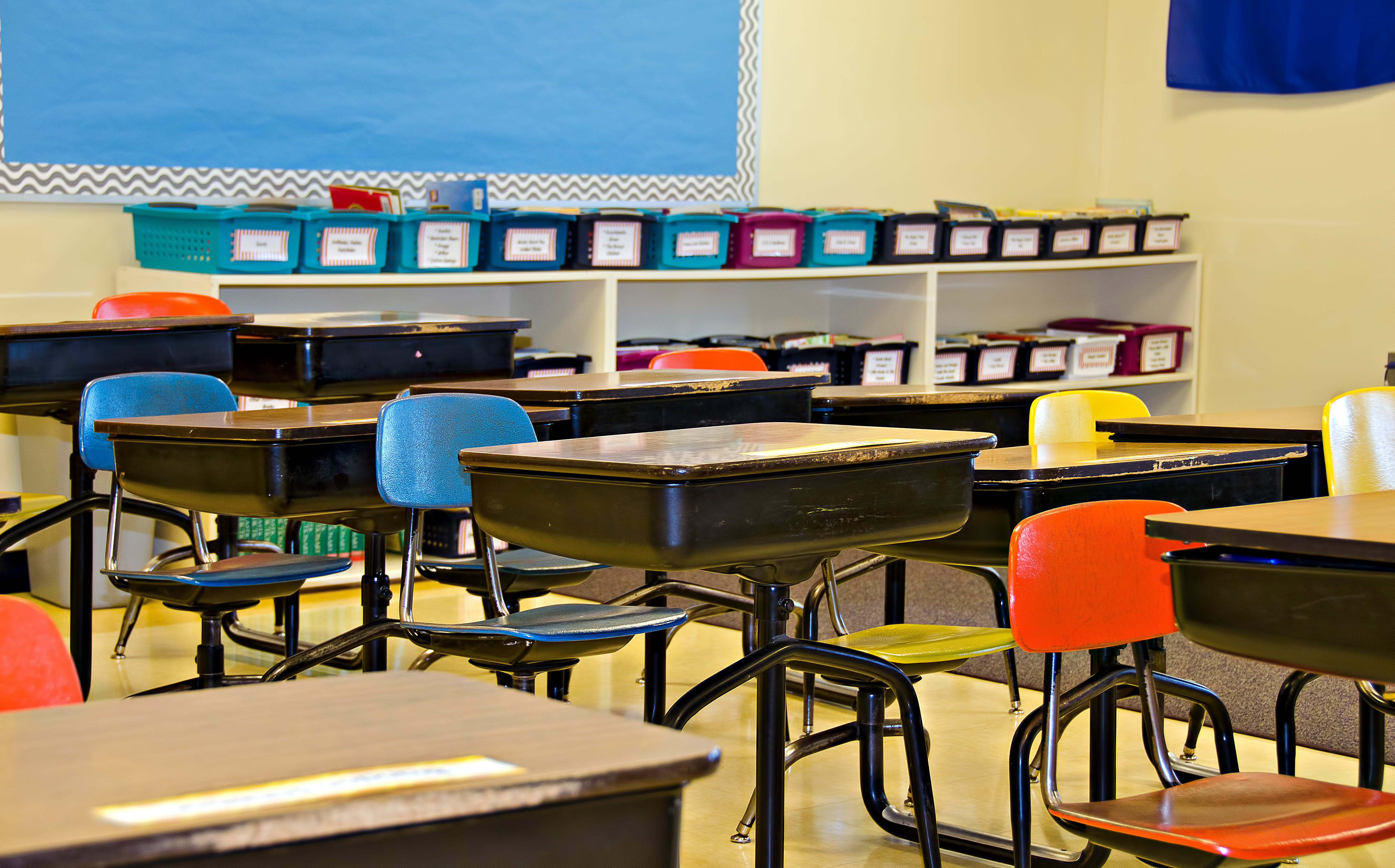 Students away from a classroom, which is filled with empty school desks.