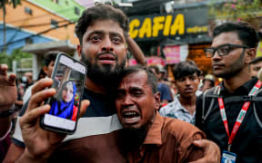 A relative wails as he shows a picture of a fire accident victim, who works as a garment factory worker, outside the chemical and garments factory in Dhaka on October 14, 2025. At least 16 people were killed after a fire blazed through a chemical and garments factory in Bangladeshi capital of Dhaka on October 14, fire authorities said. (Photo by AFP)