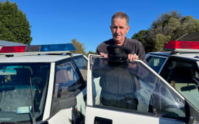 Glen Cockroft holds an old MOT hat beside one of the patrol cars
