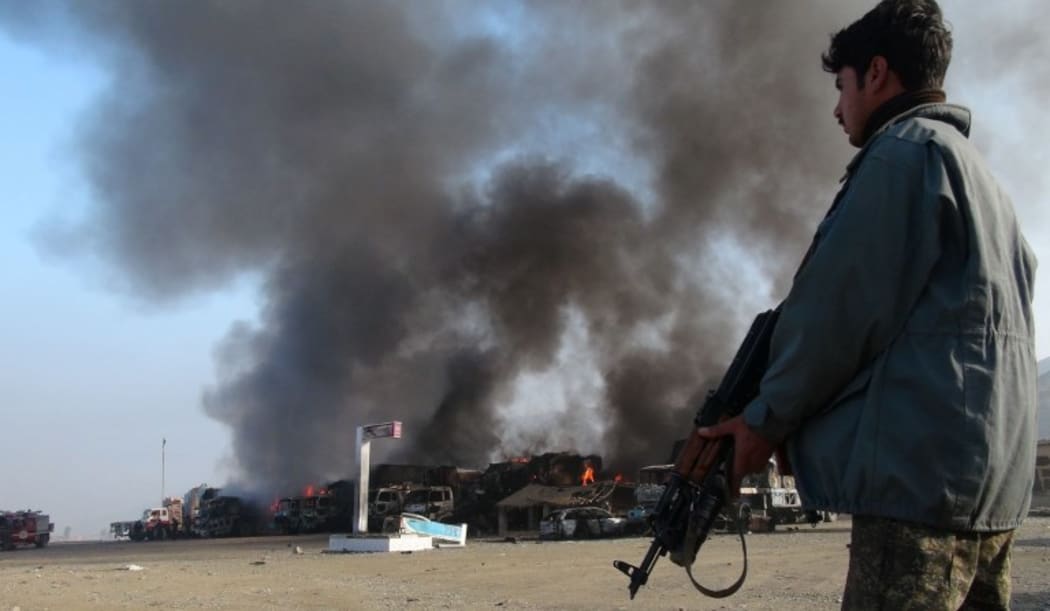 Afghan security personnel stand alert near burning NATO military vehicles after a clash between Taliban and Afghan security forces in 2013.