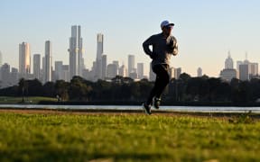 With the Melbourne skyline in the background, a jogger takes part in an early morning fun run around Albert Park Lake as Melbourne awoke to freezing conditions on July 3, 2024. (Photo by William WEST / AFP)