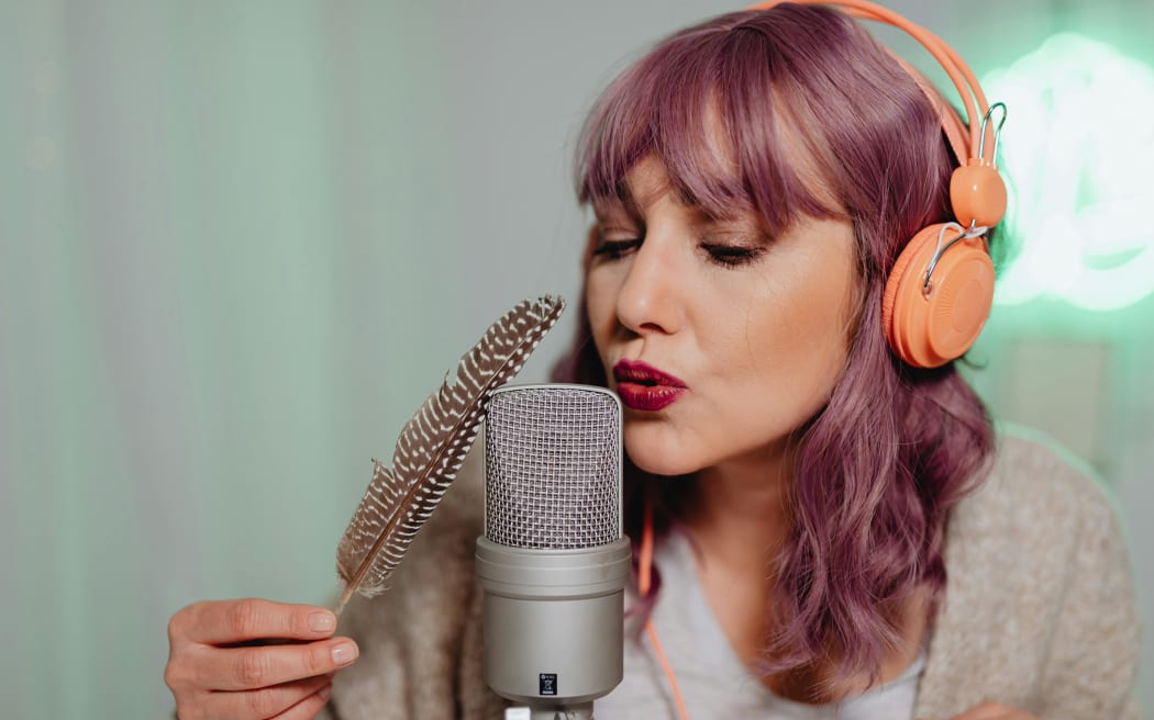 A woman with pink hair blows into a microphone.