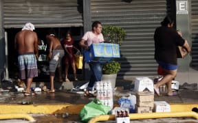 People collect groceries in a looted supermarket after the passage of Hurricane Otis in Acapulco, Guerrero State, Mexico, on October 26, 2023. Hurricane Otis killed at least 27 people as it lashed Mexico's beach resort city of Acapulco as a scale-topping category 5 storm, officials said Thursday, in what residents called a "total disaster." (Photo by RODRIGO OROPEZA / AFP)