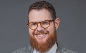 Craig McCulloch smiling wearing a suit and glasses