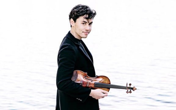 Violinist Benjamin Beilman carrying his violin beside calm water