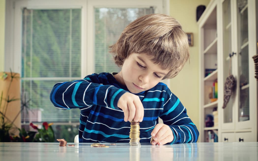 A photo of a little boy making stack of coins, counting money at table. Learning financial responsibility and planning savings concept.