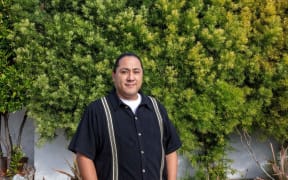 Frankie Guzman stands in front of a concrete wall covered in green plants. He's smiling at the camera.