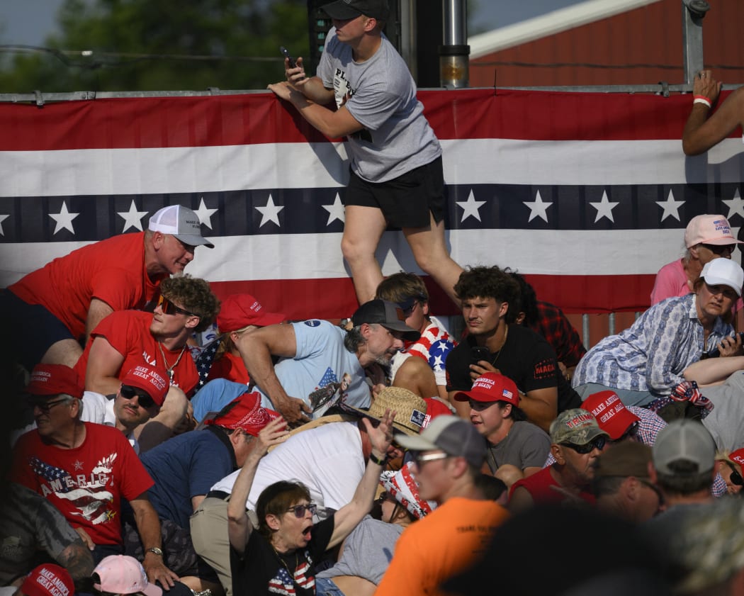 BUTLER, PENNSYLVANIA - JULY 13: Attendees duck from gunfire at a campaign rally for Republican presidential candidate, former U.S. President Donald Trump at Butler Farm Show Inc. on July 13, 2024 in Butler, Pennsylvania. Trump slumped before being whisked away by Secret Service with injuries visible to the side of his head. Butler County district attorney Richard Goldinger said the shooter and one audience member are dead and another was injured.