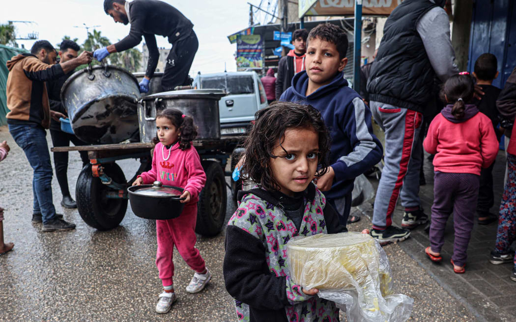 Displaced Palestinian children carry rations of red lentil soup, distributed by volunteers in Rafah in the southern Gaza Strip on February 18, 2024, amid the ongoing conflict between Israel and the militant group Hamas. After more than four months of war that has flattened huge swathes of the Strip, Gazans are inching closer towards famine, according to the UN's World Food Programme. (Photo by SAID KHATIB / AFP)