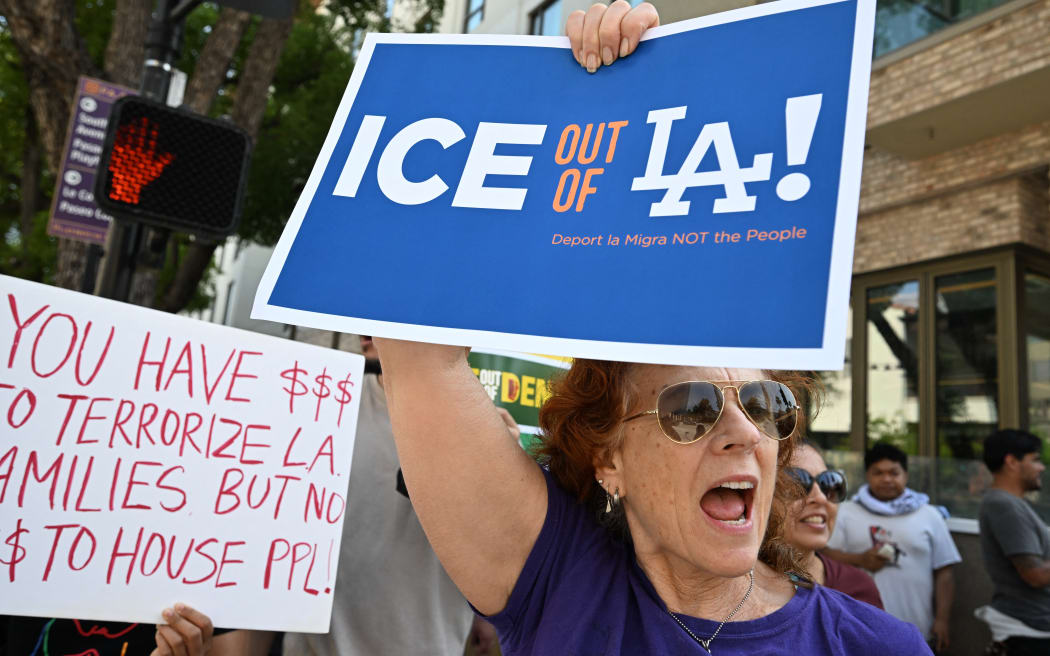 Protestors holding signs reading "ICE ot of LA!" march in front of the AC Hotel Pasadena on June 8, 2025, in Pasadena, California, as they believe ICE agents are staying at this hotel. US President Donald Trump deployed 2,000 troops on June 7 to handle escalating protests against immigration enforcement raids in the Los Angeles area, a move the state's governor termed "purposefully inflammatory." Federal agents clashed with angry crowds in a Los Angeles suburb as protests stretched into a second night Saturday, shooting flash-bang grenades and shutting part of a freeway amid raids on undocumented migrants, reports said. (Photo by Robyn BECK / AFP)
