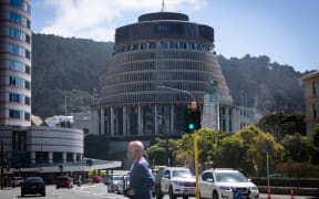 A man wearing a mask crosses the street in front of Parliament
